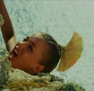 A woman with a blonde mohawk dangles from a cliff edge.