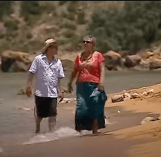 A man and woman walk along the shoreline of a sandy beach.