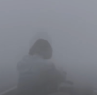 A man in a small wooden dinghy, surrounded by fog.