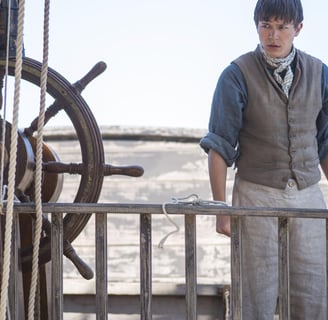 A teenage boy stands on the deck of a sailing ship.