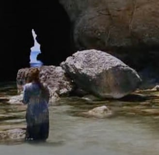 A woman stands in water amongst rocks.