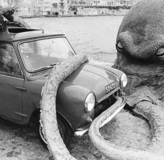 A 1960s mini parked on beach next to a giant octopus.