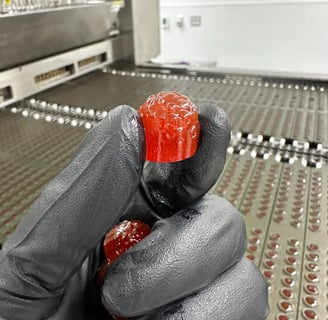 a person's hand holding a red gummy in front of automated gummy machine