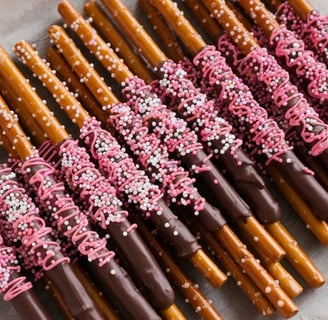 Long pretzel rods dipped in milk chocolate, decorated with pink and white sprinkles, neatly displaye