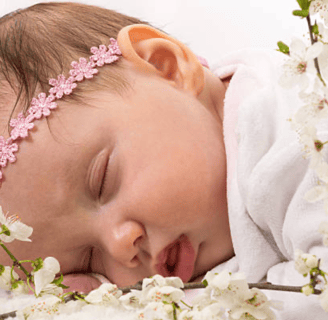 a baby lying on her front, wearing garland of flowers around her head