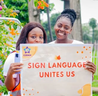 2 women smiling while holding a banner that says "Sign language unites us"