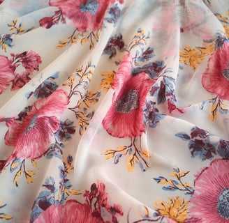 A photo of a printed polyester chiffon fabric. The fabric has a floral pattern in shades of pink, blue, and yellow on a white