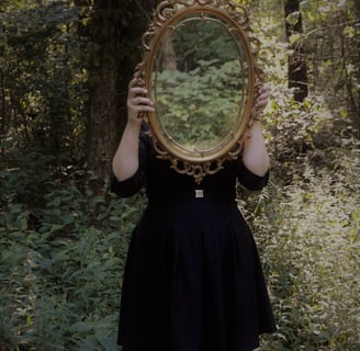 Woman holding mirror in forest, reflecting the sacred field of relationship and unseen inner truths