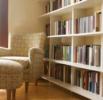 uma cadeira em frente a uma estante de livros ao lado de uma janela