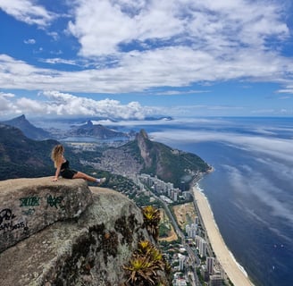 imagem com uma mulher sentada na beira da pedra da Gávea no Rio Janeiro