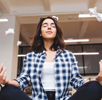 Relaxing time joyful young woman having meditation on table in office surround flying papers.