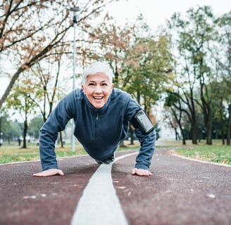 a woman with short white hair and running clothes is doing a push up outside in a park path
