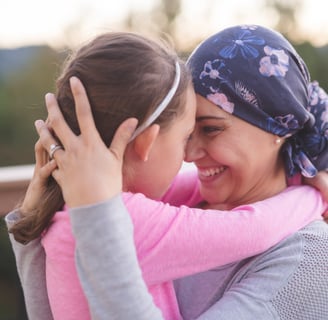 a smiling woman in a purple head wrap and a girl in a pink shirt embracing