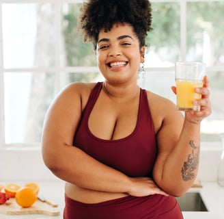 a woman in a red top and yoga pants is holding a glass of orange juice