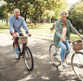 an older man and woman riding bicycles in a park