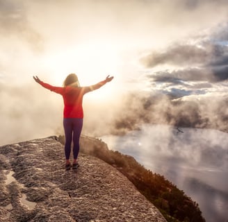 a person is standing on cliff with her arms outstretched out to the sky