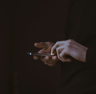 A person wearing a dark long-sleeved shirt is using a smartphone in a dimly lit environment.