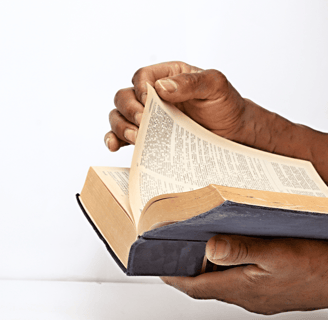A pair of hands holding and flipping through the pages of an old, well-worn book, possibly a Bible.