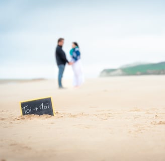 Un couple sur une plage de sable blanc face à face avec une ardoise au premier plan