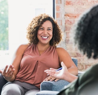 a woman sitting on a couch talking to another woman 