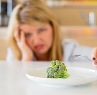 a woman sitting at a table with a plate of broccoli