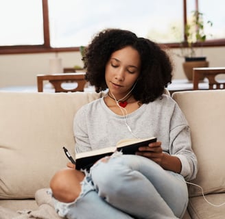 a woman sitting on a couch with headphones journaling in a notebook on