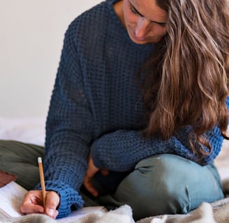 a woman sitting on a bed with a notebook and a pen