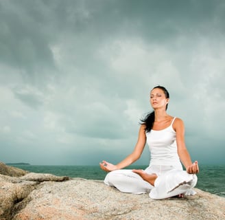 woman meditating on a rock by the ocean