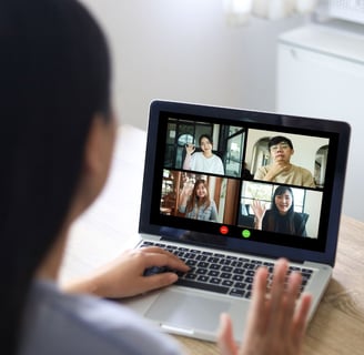 a woman sitting at a table with a laptop computer screen showing a video call