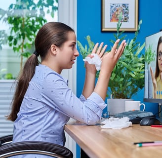 a woman sitting at a desk with a computer screen showing a video chat