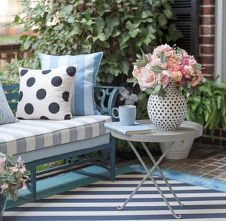 A striped outdoor rug paired with polka-dot cushions on a bench, with a small table featuring a patt