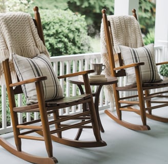 Two wooden rocking chairs with knitted throws and patterned cushions, positioned around a small roun