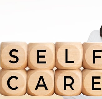 a woman sitting with a wooden block with the words self care