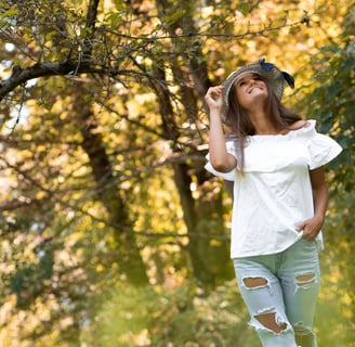 a woman in ripped jeans and a white top walking in the woods