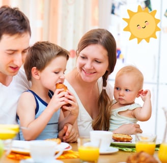 a family sitting at a table with a baby and a boy eating a sandwich