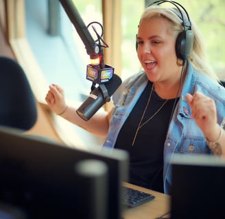 A blonde haired person with headphones on smiling into a microphone in a recording studio