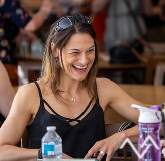 Lady laughing sitting at a table she has sunglasses on her head
