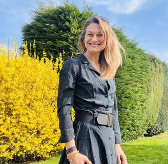 Caroline stood outside on a sunny day by hedgerows she is smiling.