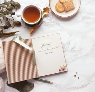 Marble table top with journal, olives and cup of tea with biscuits on a plate.
