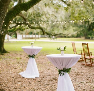 Mesa de coctel decorada para boda al aire libre, con mantel y decorascion floral
