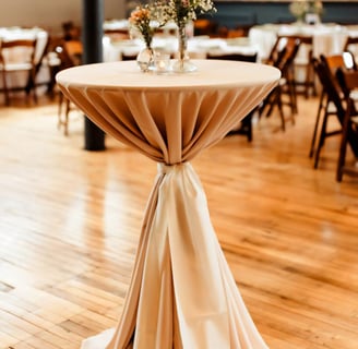 Mesa de coctel en un salon decorada con un mantel y flores