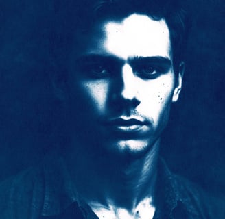 Close-up portrait of a young man with a serious expression, defined features, and short wavy dark ha