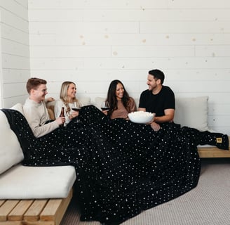a group of 4 friends enjoying a drink together under one big extra large blanket