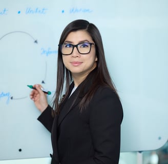 Ka Ming Zwingenberger in a suit and glasses standing in front of a white board with a marker..