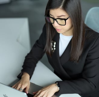 Ka Ming Zwingenberger in a suit and glasses is typing on a laptop on a desk.