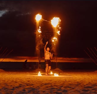 a man throws flaming torches in the air on a beach in Bang Tao Thailand