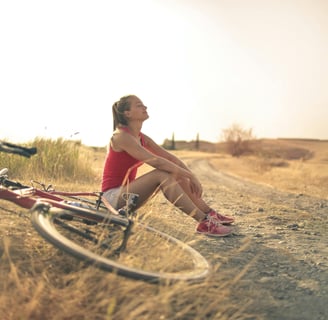 Woman with bicycle resting on countryside road in sunlight. Photo by Andrea Piacquadio on Pexels.