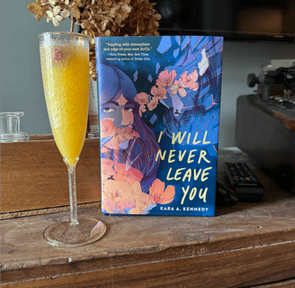 A hardcover copy Kara A. Kennedy's novel I WILL NEVER LEAVE YOU standing next to a mimosa glass