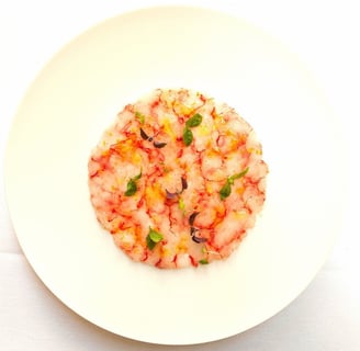 Un plato blanco con un carpaccio de gambas en forma circular