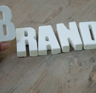 Palavra brand feita de plástico sobre uma superfície de madeira. Uma mão segura a letra B de Brand.